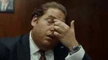 a man in a suit and tie is rubbing his forehead with his hand .