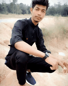 a young man wearing a watch is squatting down on a dirt hill