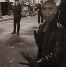 a woman in a leather jacket is standing on a street