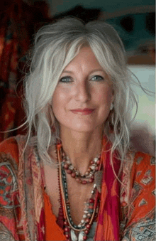 a woman with gray hair and blue eyes is wearing a necklace and a scarf .