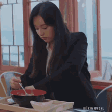 a woman in a suit is sitting at a table with a bowl of food and a spoon in her hand .