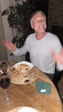 a man is sitting at a table with a bowl of food and a glass of wine