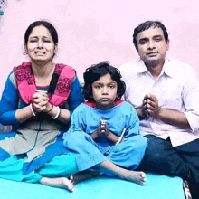 a man and a woman are sitting next to a little girl who is sitting on a bed with her legs crossed .