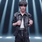 a man in a leather jacket and studded belt stands in front of a blue light