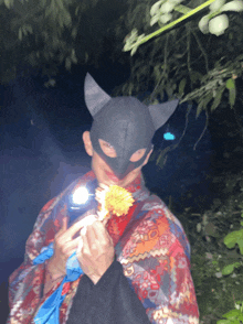 a person wearing a cat mask holds a flower