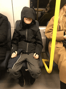 a boy wearing a hooded jacket is sitting on a train