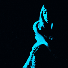 a woman with long blonde hair is sitting in a dark room with a blue light behind her