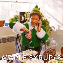 a man in a green elf costume is talking on a cell phone while pouring maple syrup into a glass .