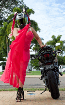 a woman in a red dress is standing next to a black motorcycle with a license plate that says adkat