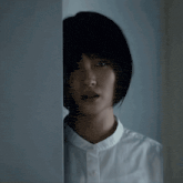 a woman in a white shirt is peeking out of a doorway