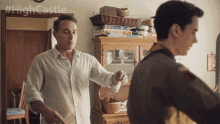 two men are standing in front of a shelf with a stack of board games on it and the hashtag #highcastle visible