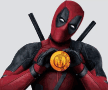 deadpool is holding a gold coin with the letter m on it in his hands .