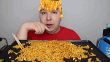 a man in a red shirt is eating noodles with french fries on his head