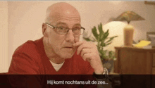 a bald man wearing glasses and a red shirt is sitting at a table