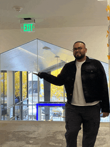 a man in a black jacket points to an exit sign