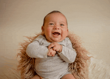 a baby in a gray bodysuit is sitting on a furry blanket and smiling