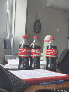 three bottles of coca cola are on a desk