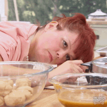 a woman with red hair is laying on a table with bowls of food and a sign that says the great american baking show