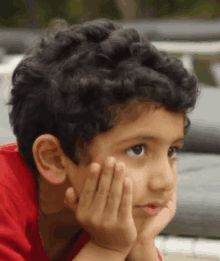 a young boy with curly hair holds his hand to his face