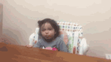 a little girl is sitting in a high chair looking at the camera .