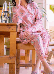 a woman in a pink floral dress is sitting on a wooden chair