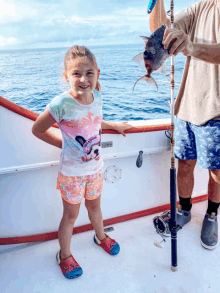 a little girl wearing a mickey mouse shirt is holding a fish on a boat