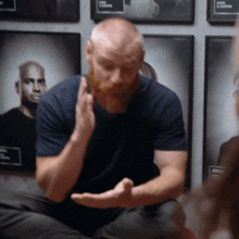 a man with a beard wearing a blue shirt is sitting in front of a wall with framed pictures of athletes