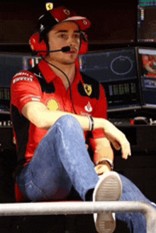 a man wearing headphones and a ferrari shirt sits on a chair