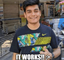 a young man wearing a t-shirt that says `` it works '' is standing in front of a building .