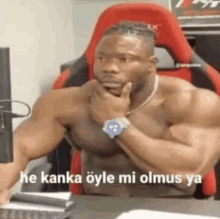 a shirtless man is sitting at a desk with his hand on his chin and looking at a computer screen .