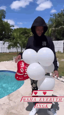 a man in a black hoodie is holding balloons and a red balloon that says " i love you "