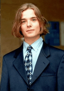 a young man wearing a suit and tie is standing in front of a wall .