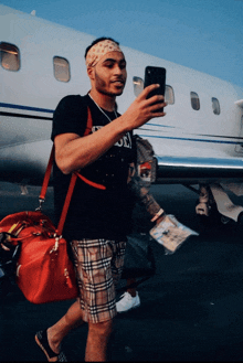 a man taking a picture of himself in front of an airplane wearing a black shirt that says ' gucci ' on it