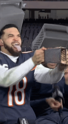 a man in a bears jersey is holding a grater and sticking his tongue out