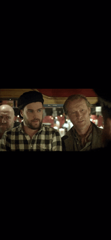 a man with a beard wearing a plaid shirt is standing next to two other men