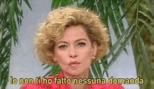 a woman with blonde curly hair is standing in front of a palm tree and says lo non ti ho fatto nessuna domanda .