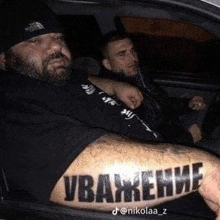 a man with a tattoo on his arm is sitting in a car with two other men .