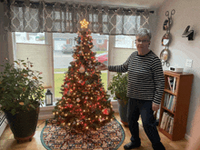 a woman stands in front of a christmas tree in a living room