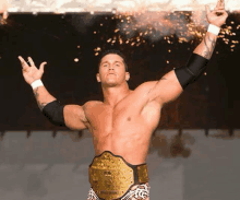 a shirtless wrestler wearing a world heavyweight championship belt is standing in front of a firework display .