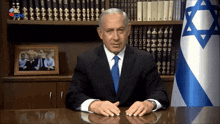 a man in a suit and tie sits at a desk in front of a flag with a star of david on it