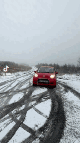 a red car is driving on a snow covered road