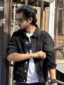 a young man wearing sunglasses and a black jacket stands in front of a fence