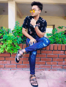 a young man is sitting on a brick wall wearing sunglasses and a watch