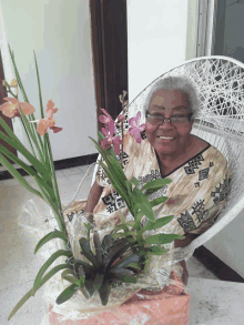 an elderly woman sits in a chair holding flowers and smiling