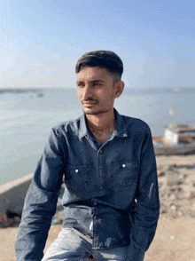 a young man in a denim shirt sits on a beach