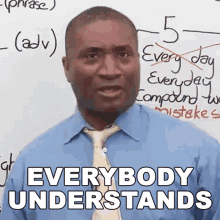 a man in a blue shirt and tie is standing in front of a white board that says everybody understands