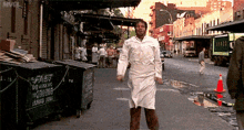 a man in a white apron is walking down a street in front of a green dumpster that says fast