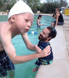 a man holds a baby in a swimming pool with a lifeguard on the shore