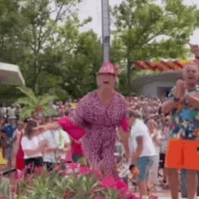 a woman in a pink leopard print dress and pink hat is dancing in front of a crowd of people .