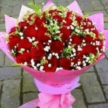 a bouquet of red roses wrapped in pink paper on a sidewalk .